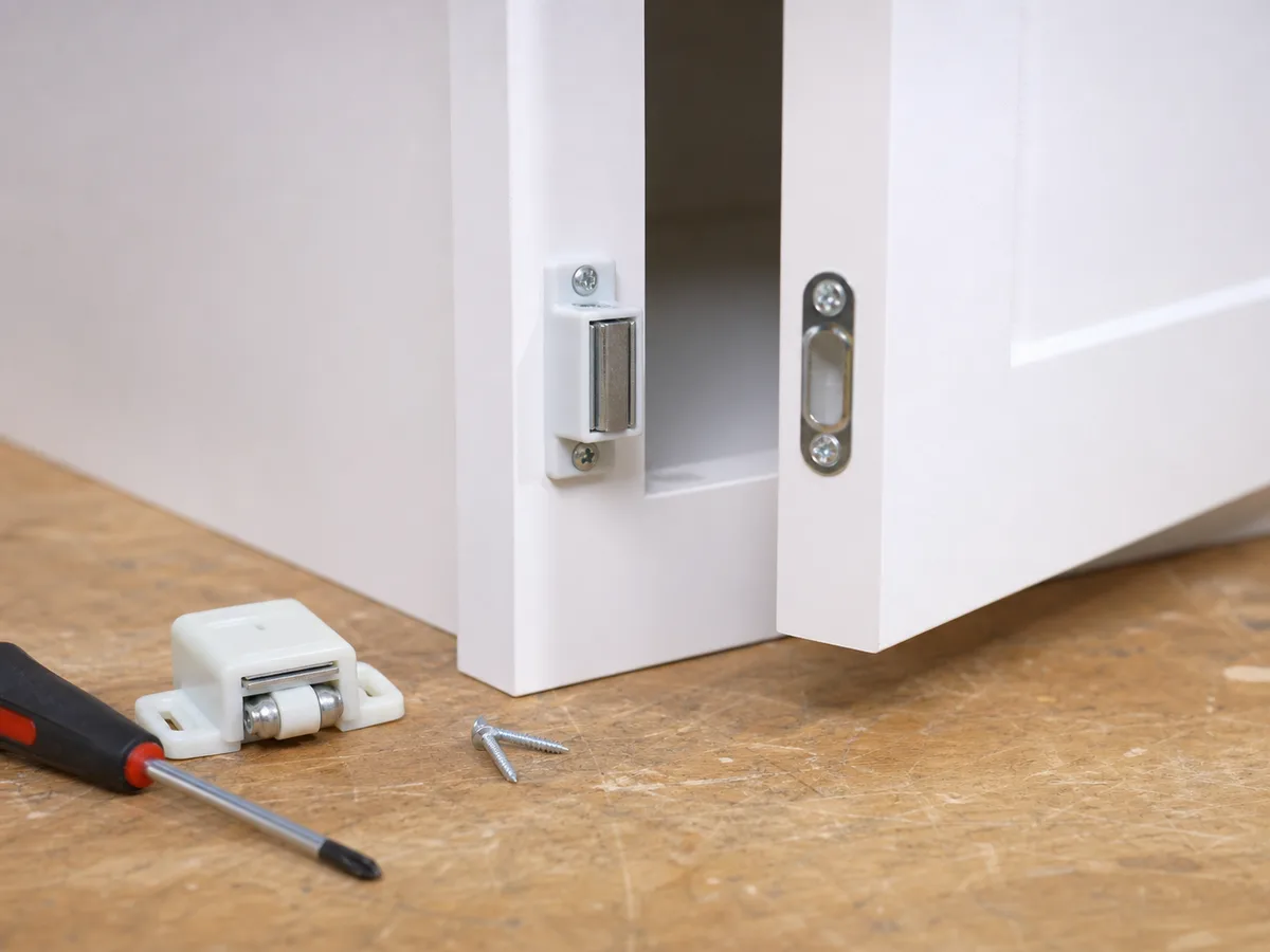 A magnetic catch and strike plate aligned on a small cabinet door sample.