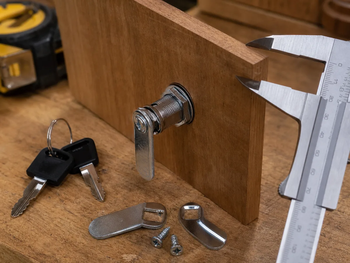 A cam drawer lock fitted through a sample panel while the panel thickness is checked.