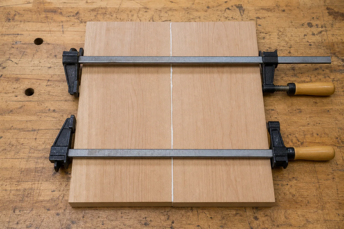 Illustrative white-glue workflow: two close-fitting bare wood boards aligned flat while bar clamps close the joint. Always follow the selected glue's instructions.
